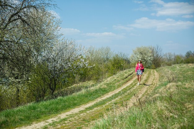 Bella ragazza in un vestito che cammina nella foresta primaverile dove fioriscono gli alberi