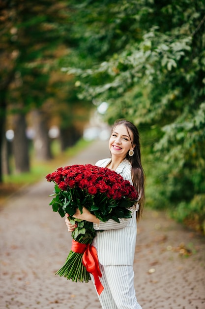 Bella ragazza in un vestito con fiori nelle mani di una rosa su uno sfondo verde