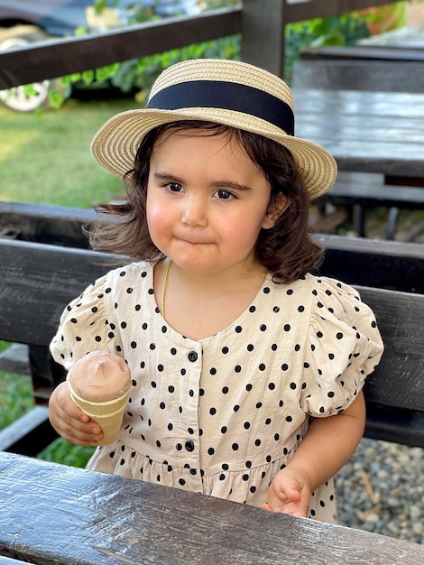 bella ragazza in un vestito con pois e un cappello mangia gelato al cioccolato, foto al telefono