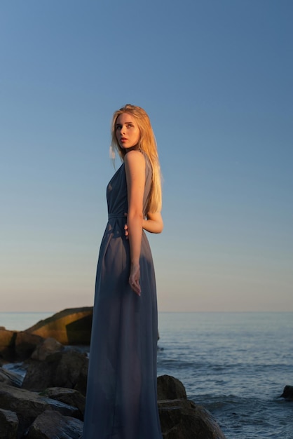 bella ragazza in un vestito grigio in riva al mare al tramonto