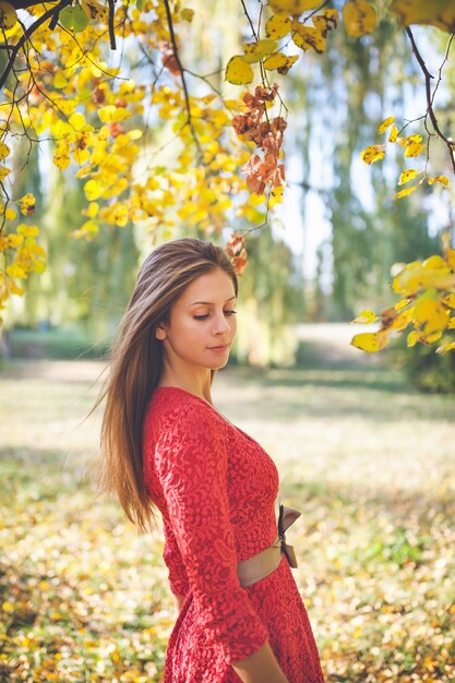 Bella ragazza in un vestito rosso in un parco di autunno