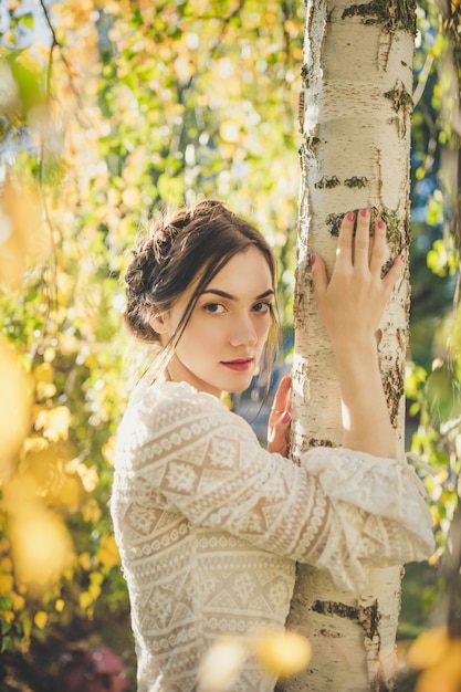 Bella ragazza in una camicetta di pizzo bianco sotto l'albero di betulla