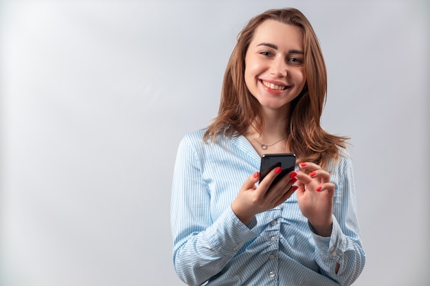 bella ragazza in una camicia blu con un telefono su uno sfondo bianco.