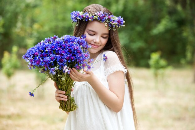 Bella ragazza in una corona di fiordalisi e con un mazzo di fiori nel cestino.