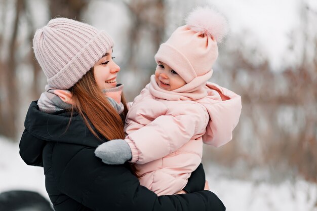 Bella ragazza in una tuta rosa che gioca con sua madre in un parco nevoso di inverno