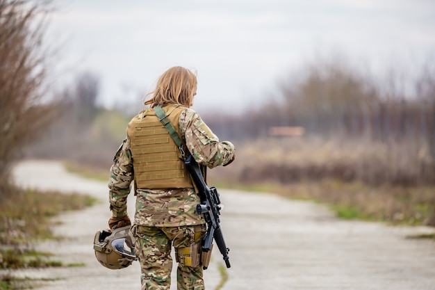 Bella ragazza in uniforme militare con una pistola di airsoft che cammina sulla strada