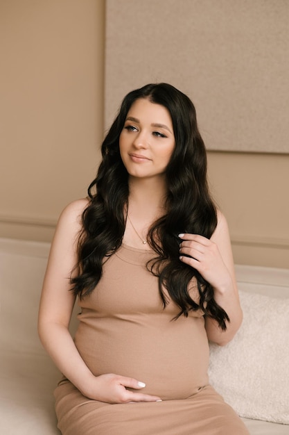 Bella ragazza incinta con riccioli in un vestito in uno studio luminoso con interni eleganti il concetto di una felice gravidanza e famiglia
