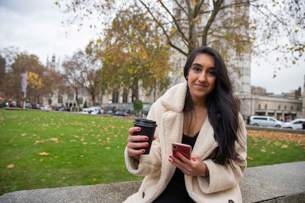 Bella ragazza indiana che si prende una pausa dal lavoro seduta su un muro nel parco pubblico