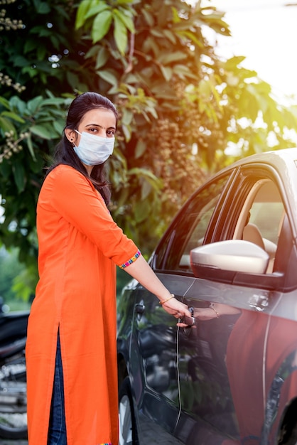 Bella ragazza indiana in maschera seduta in macchina, maschera protettiva contro il coronavirus, autista in una strada cittadina durante la pandemia di covid-19