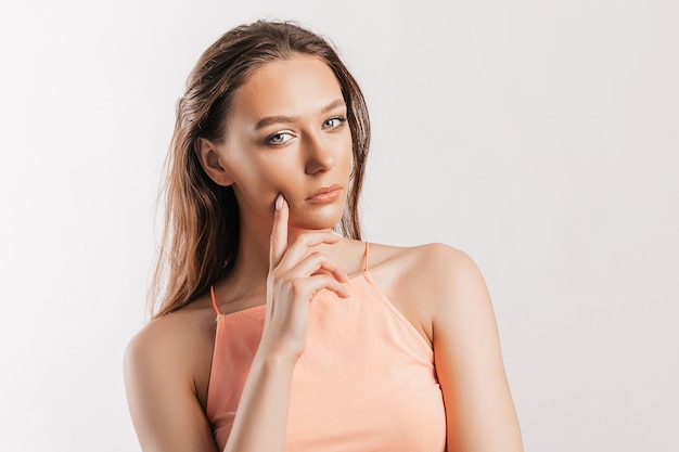 Bella ragazza infelice cipiglio e pensa su sfondo grigio isolato. La donna seria guarda di lato e tiene la mano sul viso