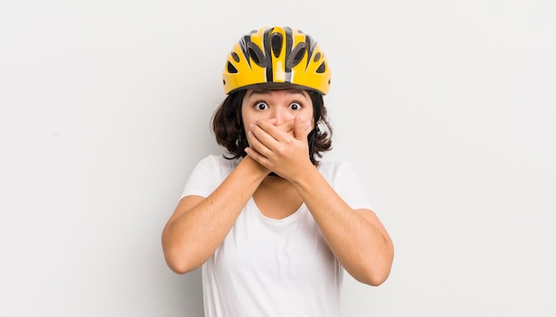 Bella ragazza ispanica che copre la bocca con le mani con un concetto di bici scioccato