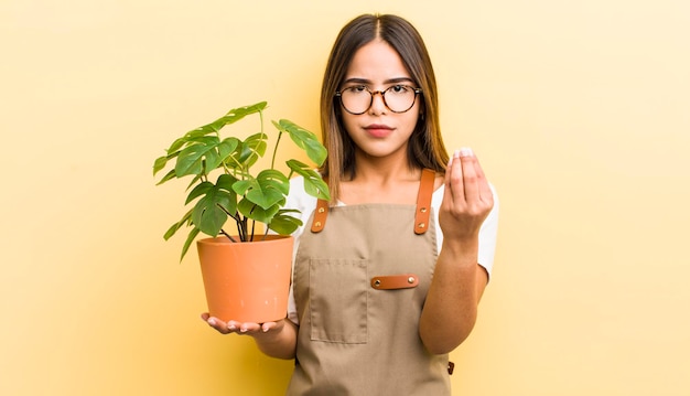 Bella ragazza ispanica che fa un gesto di capice o denaro che ti dice di pagare il concetto di pianta