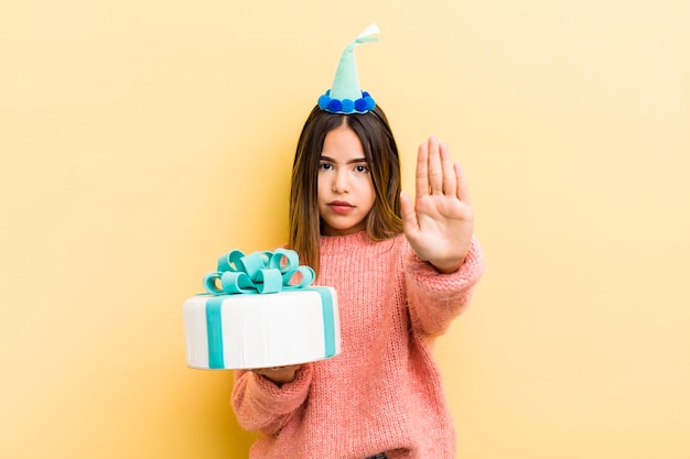 Bella ragazza ispanica che sembra seria mostrando il palmo aperto facendo il concetto di compleanno di gesto di arresto