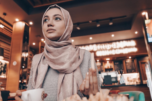 Bella ragazza musulmana in hijab che pranza in un bar accogliente e sorride