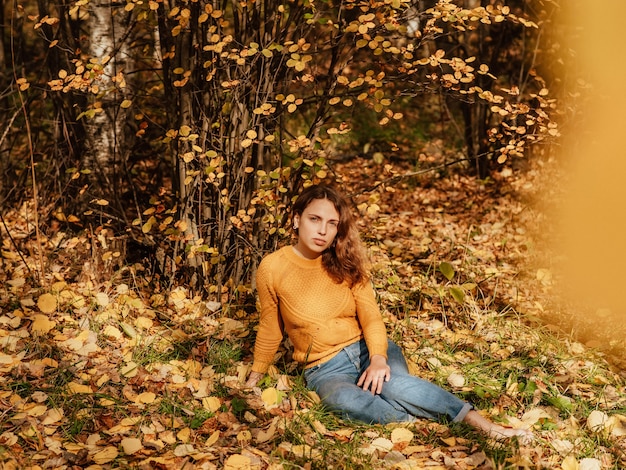 Bella ragazza nel parco autunnale seduto sulle foglie cadute