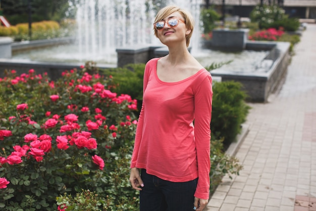 Bella ragazza nel parco. Rose in fiore. Fontana.