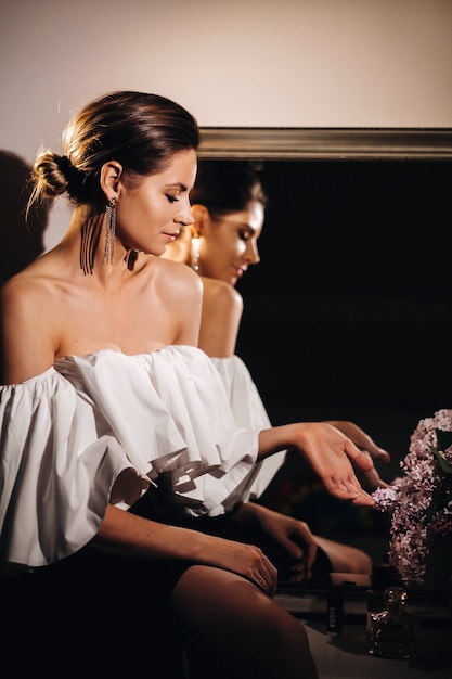 Bella ragazza nello specchio riflesso a casa. Ragazza prima delle vacanze vicino allo specchio di casa Una ragazza in abito bianco con i capelli lunghi sta andando a una festa a casa.