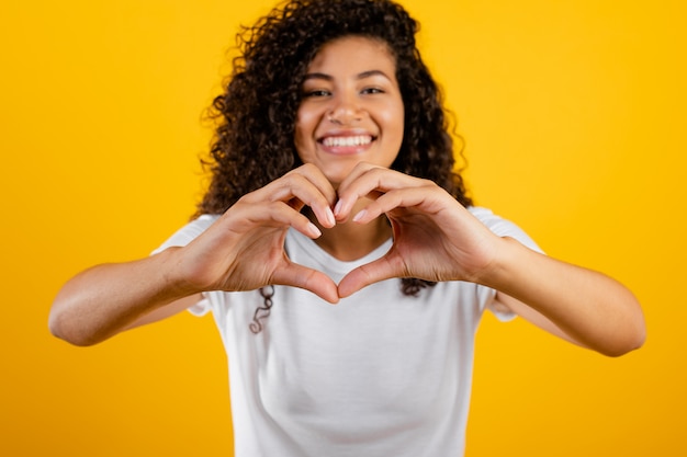 Bella ragazza nera felice che mostra cuore con le mani isolate sopra giallo