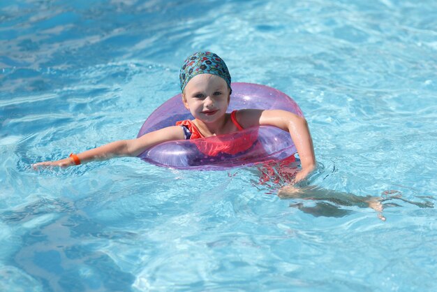 Bella ragazza nuotare nella piscina blu con anello gonfiabile.