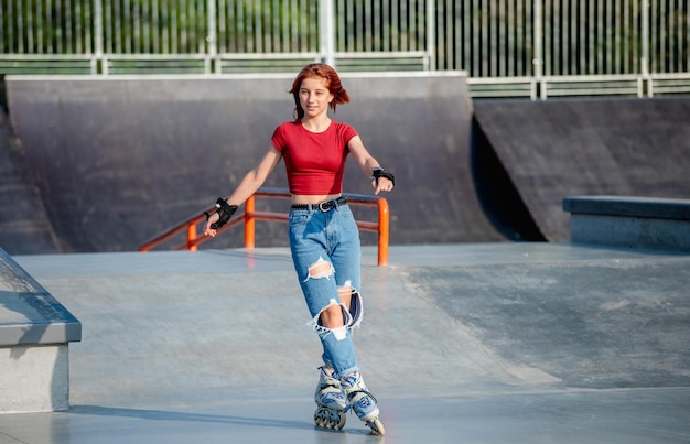 Bella ragazza pattinaggio a rampa del parco in una giornata di sole. Adolescente di sesso femminile che indossa rulli che guidano all'aperto in estate