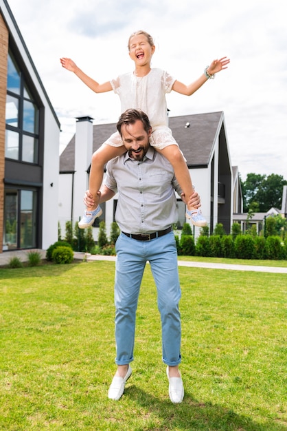 Bella ragazza piacevole seduta sulle spalle di suo padre pur avendo paura dell'altezza