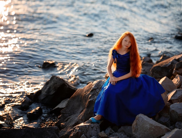 Bella ragazza romantica con i capelli rossi saluta l'alba in riva al mare