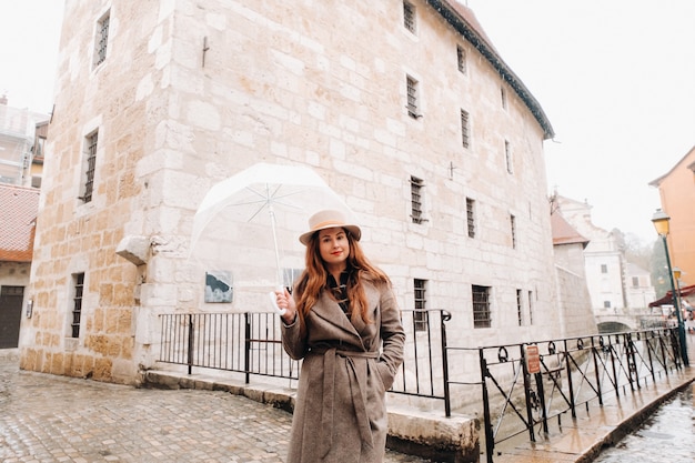 Bella ragazza romantica in un cappotto e un cappello con un ombrello trasparente ad Annecy. Francia. La ragazza con il cappello in Francia.