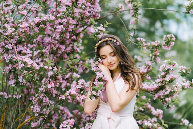 bella ragazza romantica in un vestito rosa delicato si erge in primavera vicino a un cespuglio di fiori rosa weigela e tocca un ramo