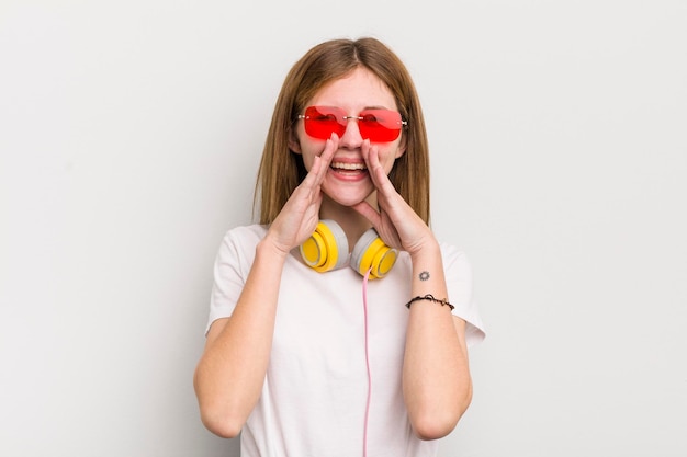 Bella ragazza rossa che si sente felice dando un grande grido con le mani accanto alla bocca ascolta il concetto di musica