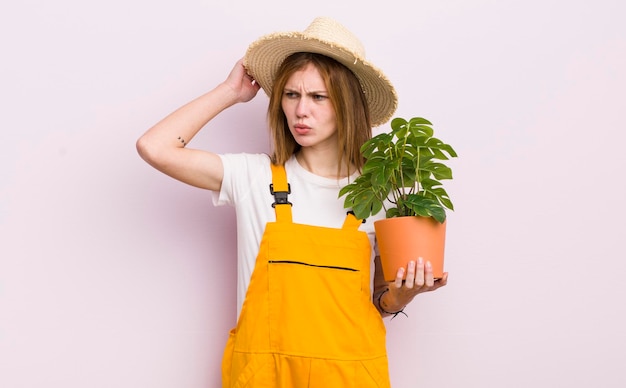 Bella ragazza rossa che si sente perplessa e confusa che graffia la pianta della testa e il concetto di giardinaggio