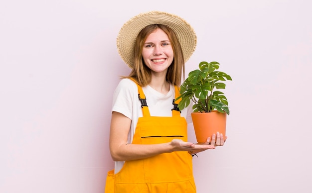 Bella ragazza rossa che sorride allegramente sentendosi felice e mostrando un concetto di pianta e giardinaggio