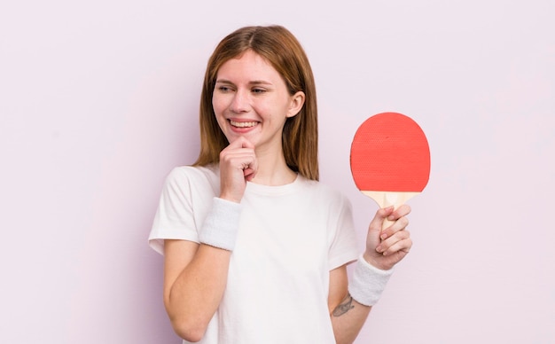 Bella ragazza rossa che sorride con un'espressione felice e sicura con la mano sul concetto di ping pong del mento