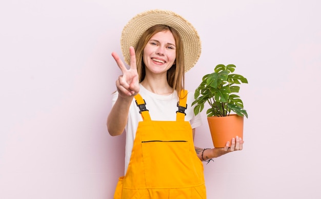 Bella ragazza rossa che sorride e sembra felice che gesturing la vittoria o la pianta della pace e il concetto di giardinaggio