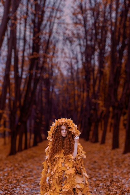 Bella ragazza rossa come un autunno nel mantello di foglie nella foresta