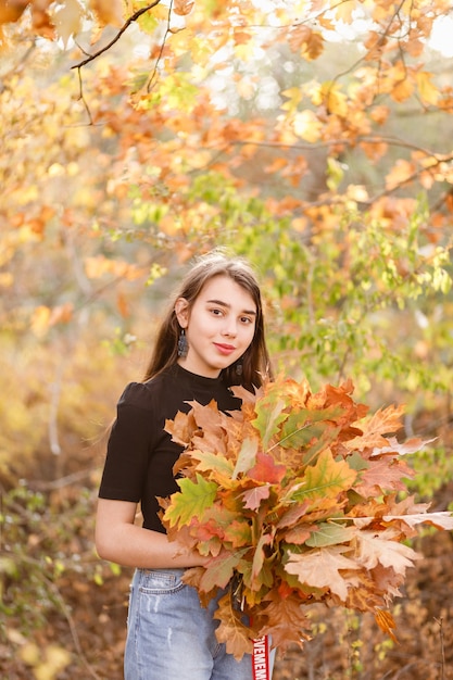 Bella ragazza rossa con un bouquet di foglie di autunno gialle