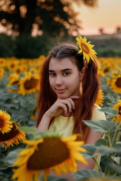 Bella ragazza rossa in una maglietta gialla su un campo con i girasoli al tramonto