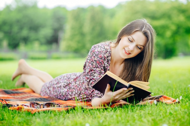 Bella ragazza sdraiata sull'erba e la lettura di un libro all'aperto nel parco