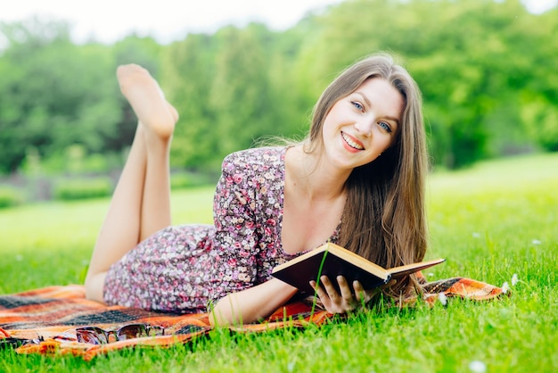 Bella ragazza sdraiata sull'erba e la lettura di un libro all'aperto nel parco