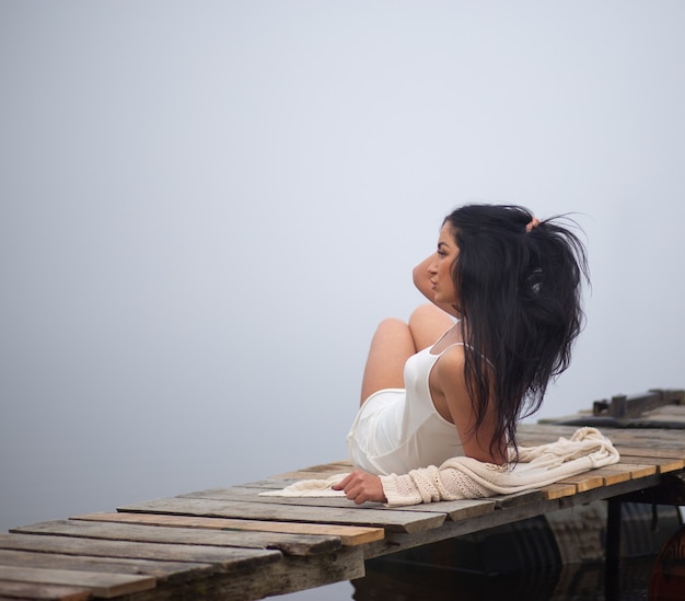 Bella ragazza seduta sul molo in riva al fiume