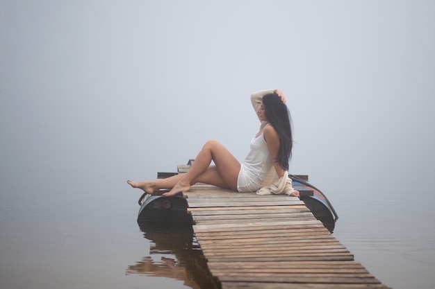 Bella ragazza seduta sul molo in riva al fiume