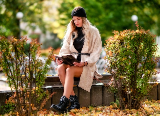 Bella ragazza seduta sulla panchina nel parco autunnale e leggendo un libro