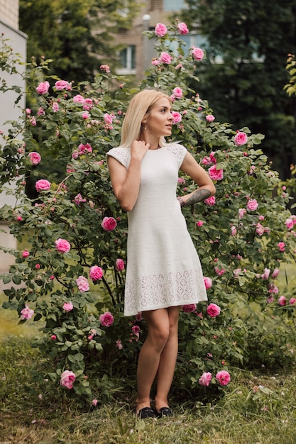 Bella ragazza sexy in bianco lavorato a maglia su uno sfondo di natura e rose in fiore