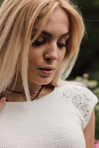 Bella ragazza sexy in bianco lavorato a maglia su uno sfondo di natura e rose in fiore