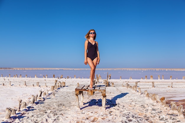 Bella ragazza sexy in costume da bagno nero in posa su un lago salato rosa. Servizio fotografico di una ragazza abbronzata su un lago rosa salato