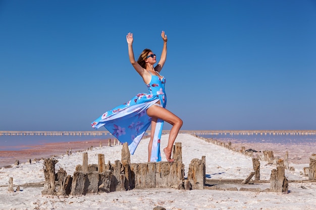 Bella ragazza sexy in un vestito blu in posa su un lago salato rosa. Servizio fotografico di una ragazza abbronzata su un lago rosa salato.