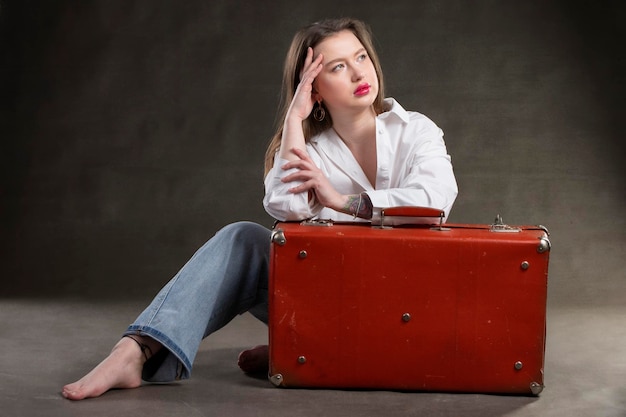 Bella ragazza si siede con una valigia vintage su uno sfondo grigio