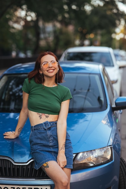 Bella ragazza si siede sul cofano di un'auto blu