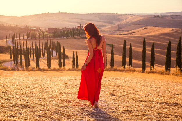 Bella ragazza snella in un vestito rosso al tramonto in Toscana, Italia