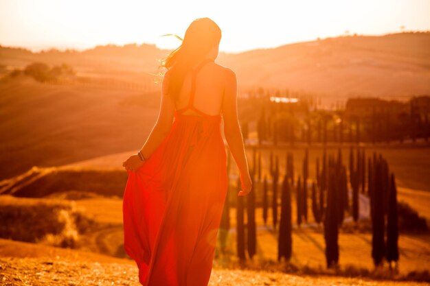 Bella ragazza snella in un vestito rosso al tramonto in Toscana, Italia