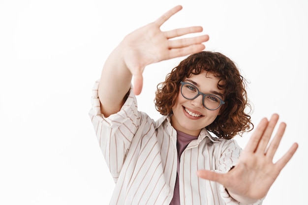 Bella ragazza sognante con gli occhiali che sembra felice attraverso il gesto delle cornici delle mani, immaginando qualcosa, sognando ad occhi aperti e immaginando un'immagine perfetta